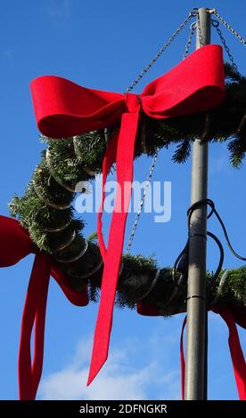 Détail d'une couronne de Noël avec branches de sapin et rubans rouges sur un poteau. Bleu ciel comme arrière-plan. Banque D'Images