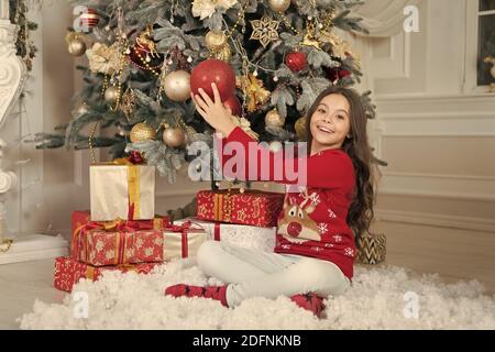 Bénéficiant d''hiver. Décor d'attributs de Noël. Petite fille près de l'arbre de Noël. Enfant célébrer Noël à la maison. Traditions d'hiver. Boutique cadeaux concept. Porter le chandail de Noël pour enfants adorables. Banque D'Images