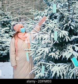 Femme près d'un arbre de Noël avec des décorations de masques de visage. Concept de problème pandémique du virus de la grippe pour la nouvelle année. Banque D'Images