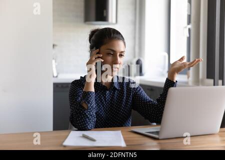 Femme hindoue millénaire parlant au téléphone et regardant l'écran d'ordinateur Banque D'Images