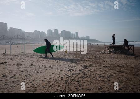 Mar del Plata, Argentine - juillet, 2020: Homme surfeur portant planche à voile sur la plage après le surf en hiver sur la plage de la ville de Mar del Plata calle Banque D'Images
