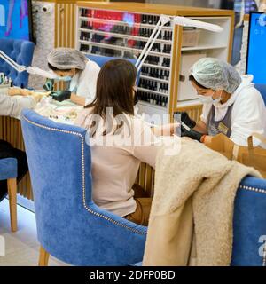 Une femme dans un masque facial obtient une manucure sur ses ongles dans un salon de beauté extérieur. Nouvelle normale, la vie pendant les vacances pendant l'épidémie - Moscou, Rus Banque D'Images