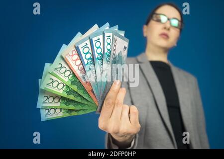 Gros plan de différentes dénominations de billets de tenge kazakhs dans la main d'une femme dans une veste et des lunettes grises. Mise au point sélective. Banque D'Images