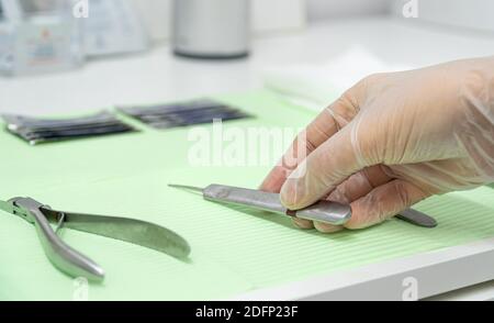 Gros plan de la main du podiatre portant des gants et prenant une gouge de la table de travail. Banque D'Images