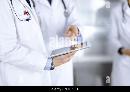 Un groupe de médecins inconnus utilise une tablette pour vérifier certains dossiers médicaux, tout en se tenant dans un bureau d'hôpital. Médecins prêts à Banque D'Images