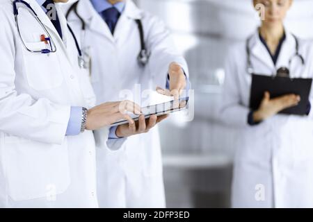 Un groupe de médecins inconnus utilise une tablette pour vérifier certains dossiers médicaux, tout en se tenant dans un bureau d'hôpital. Médecins prêts à Banque D'Images