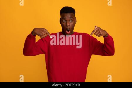 Choqué Afro-américain Guy pointant du doigt vers le bas, posant sur fond jaune Banque D'Images