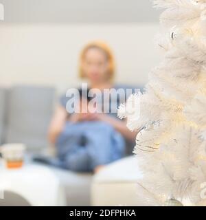 Image hors foyer d'une jeune femme gaie assise à l'intérieur canapé dans le salon de la maison utilisant les médias sociaux sur le téléphone pour le chat vidéo et rester Banque D'Images