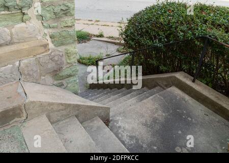 Escaliers en béton descendant autour d'un coin extérieur d'un bâtiment fait de calcaire vert en ruine, mains courantes noires sur une pente raide, horizontal comme Banque D'Images