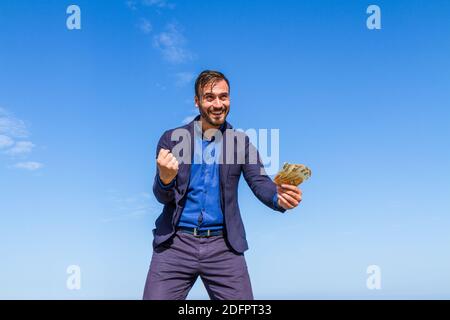 Gai attrayant barbu jeune homme tenant 50 billets en euros souriant heureux isolé sur fond bleu ciel. Banque D'Images