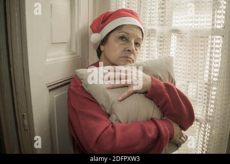 Femme âgée ayant Noël triste seule - femme mature à la retraite 60s ou 70s dans le chapeau du Père Noël déprimé et émotionnel à la maison se sentant seul et mélanque Banque D'Images