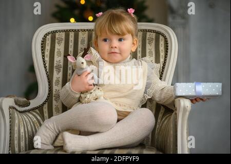 Petite fille drôle ayant le plaisir dans une chaise à l'avant De l'arbre de Noël Banque D'Images