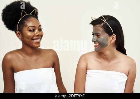 Deux jeunes belles amies sourient. Un masque est appliqué à leur visage. Procédures d'esthéticienne. Soin du visage, serrage des pores et hydratation Banque D'Images