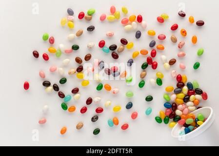 Des jelly beans débordent d'une tasse en mousse blanche sur fond blanc, composition festive et colorée avec candie, prise de vue au-dessus avec une sensation dynamique Banque D'Images