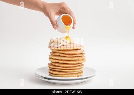 Femme versant du miel sur de savoureuses crêpes à la banane sur l'assiette contre arrière-plan blanc Banque D'Images