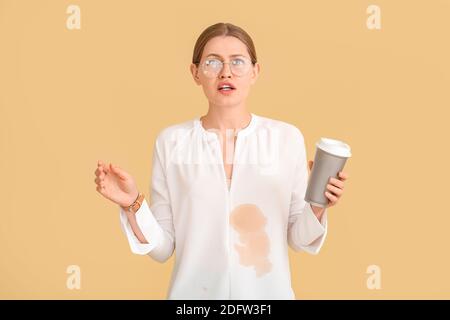 Jeune femme stressée avec taches de café sur sa chemise couleur de fond Banque D'Images