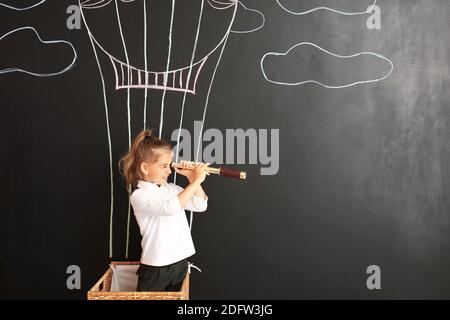 Jolie petite fille regardant dans le spyglass sur le mur noir avec ballon à air chaud dessiné Banque D'Images