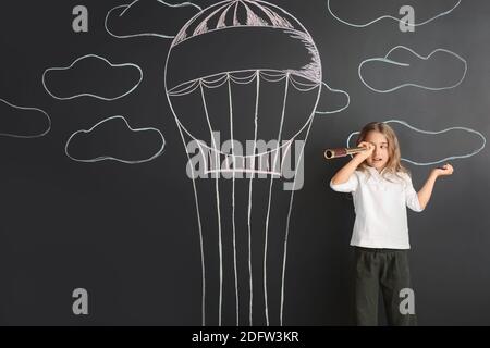 Jolie petite fille regardant dans le spyglass sur le mur noir avec ballon à air chaud dessiné Banque D'Images