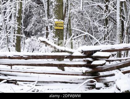 Un panneau d'intrusion de chasse interdit sur un arbre forestier au-dessus d'une clôture de rail fendu recouverte de neige pendant une tempête de neige. Banque D'Images