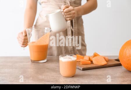 Femme préparant un délicieux smoothie à la citrouille à table Banque D'Images