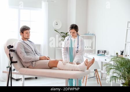 Médecin mettant la jambe cassée du jeune homme dans le plâtre Banque D'Images