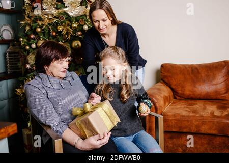 Grand-mère embrassant et donnant à sa petite-fille un cadeau de Noël. Concept de famille heureux. Banque D'Images