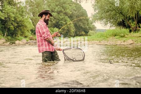 Pêche à la baissière. Pêcheur barbu dans l'eau. Activités de loisir et de sport. Pothunter. Week-end d'été. Pêche au gros gibier. Pêcheur avec canne à pêche. Homme mature pêche à la mouche. Homme attrapant le poisson. Banque D'Images