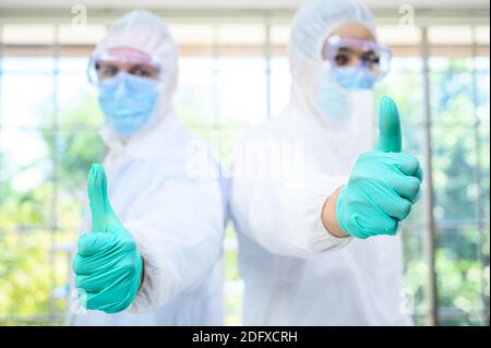 Couple de scientifiques mâles portant une combinaison de protection montrant le pouce vers le haut et se tenir sur le fond en verre au laboratoire. Portrait du scientifique Banque D'Images