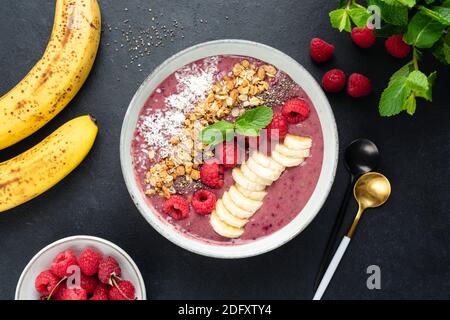 Bol à smoothie aux fruits rose vegan avec diverses garnitures supraalimentaires sur fond de béton noir. Smoothie aux framboises vibrantes Banque D'Images