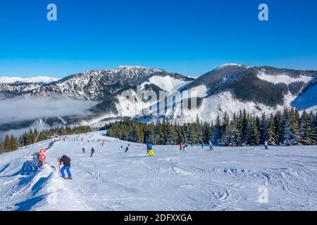 Montagnes d'hiver. Grande et douce pente de ski par temps ensoleillé. Beaucoup de skieurs. Brouillard léger dans la vallée Banque D'Images
