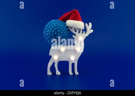 Scène de cerf de Noël avec molécule de virus bleu et chapeau de père Noël rouge. Concept de vacances pendant une pandémie de covid isolée sur fond bleu Banque D'Images