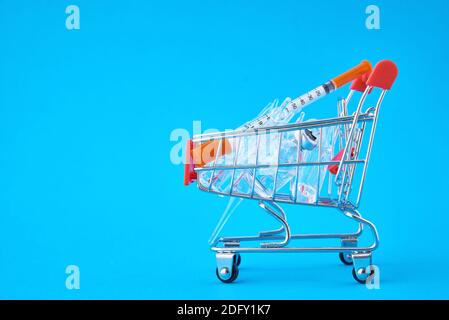 Seringues et ampoules avec médicaments dans un panier sur fond bleu. Achat de médicaments cocept Banque D'Images