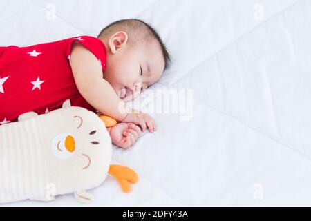 Portrait de beau nouveau-né asiatique petit bébé dormant sur un lit blanc à la maison, bébé heureux porte une chemise rouge relaxant oreiller dans la chambre, famille Mornin Banque D'Images