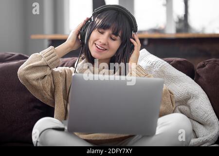 Une superbe brunette dans un casque sourit et écoute de la musique avec les yeux fermés. Banque D'Images