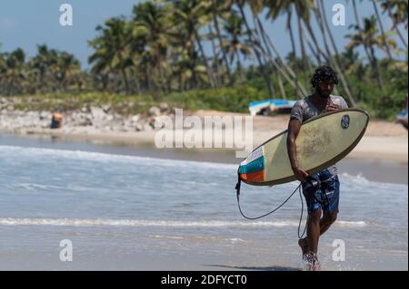 VARKALA, INDE - 14 mars 2020 : un mâle indien avec son surf à pied au bord de la mer Banque D'Images