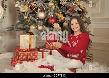 Mes vacances d'hiver parfait. Petite fille près de l'arbre de Noël. Enfant célébrer Noël à la maison. Traditions d'hiver. Boutique cadeaux concept. Porter le chandail de Noël pour enfants adorables. Décor d'attributs de Noël. Banque D'Images