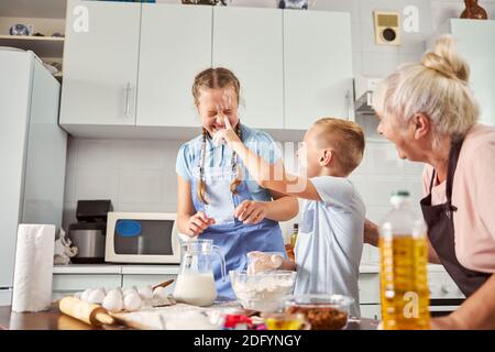 Des enfants joyeux se maculage de la farine sur les autres visages dans la cuisine Banque D'Images