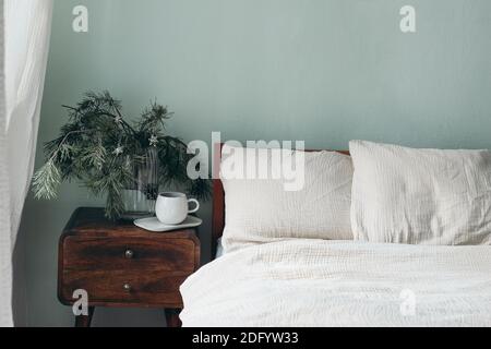 Noël encore la vie. Tasse de café, table de chevet rétro en bois. Branches de pin et décorations étoiles argentées dans un vase en verre. Lit en coton beige Banque D'Images
