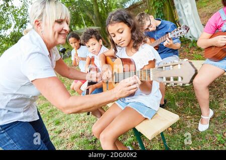 L'enseignant aide les enfants à apprendre à jouer de la guitare en classe à camp d'été ou camp d'été Banque D'Images