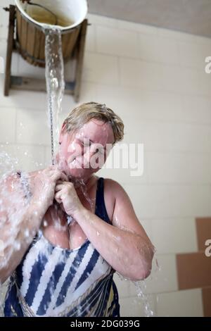 Femme versant un seau d'eau sur elle-même après le sauna Banque D'Images