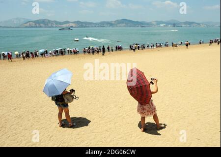 Bénéficiant d chinois, à la plage de l'île de Gulangyu à Xiamen. Les gens à rester près de l'eau, protéger les thmeselves avec parasols. En premier plan deux personnes tak Banque D'Images