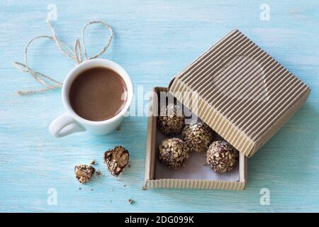 Bonbons au beurre d'arachide, glaçage au chocolat et chapelure dans une boîte de fête avec une tasse de café sur fond bleu, mise au point sélective. Délique Banque D'Images