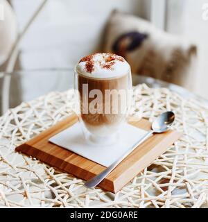Café au lait chaud ou Cappuccino sur une table dans un café ou Cuisine près de la fenêtre.café du matin Latte au lait et au chocolat sur le dessus en verre à double paroi Banque D'Images