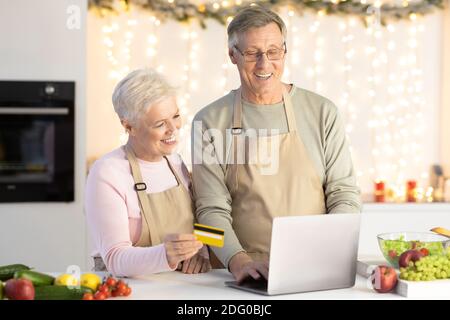 Couple âgé Shopping en utilisant un ordinateur portable et une carte de crédit dans la cuisine