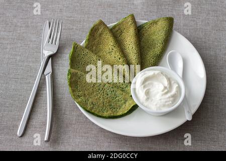 Crêpes d'épinards avec sauce au fromage cottage sur une assiette blanche sur fond gris. Délicieux petit déjeuner sain Banque D'Images