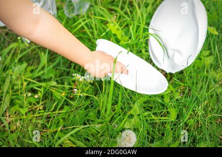 La main de l'enfant nettoie le parc des ustensiles en plastique dans l'herbe dans le parc Banque D'Images