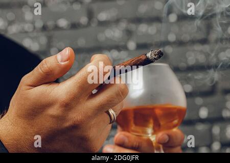 Homme tenant un verre de whisky et allumé la cigarette les mains en gros plan Banque D'Images