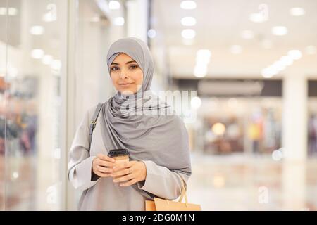 Portrait à la taille haute d'une jeune femme du Moyen-Orient portant un foulard et regardant l'appareil photo tout en appréciant les magasins dans le centre commercial, l'espace de copie Banque D'Images