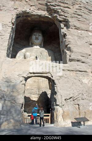 Grottes de Yungang près de Datong dans la province du Shanxi, en Chine. Grande statue de Bouddha dans une grotte à Yungang. Bouddha debout avec des personnes méconnues. Banque D'Images