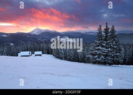 Un lever de soleil incroyable. Forêt d'hiver. Vieux cabanes en bois sur la pelouse recouverte de neige. Hautes montagnes aux sommets enneigés. Fond d'écran. Emplacement pl Banque D'Images